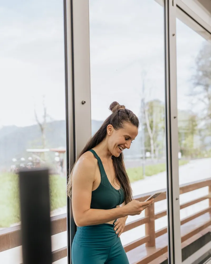 Mulher sorrindo com o celular na mão na academia